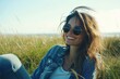© Olena - Carefree Smiling Woman in Torn Clothes Enjoying a Sunny Day on the Beach, Relaxing on Grassy Field with Sunglasses