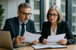 © A.Ex - people reviewing paperwork together, focused on a laptop screen.