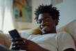 © Pixel Soul - Man with afro smiling while looking at a phone lying on a couch in a bright and airy room