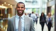 © Mey - A smiling young man in a suit standing in a modern office hallway.