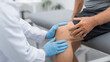 © tong2530 - Medical professional wearing gloves assessing knee joint of seated patient, clinical office with examination bed and clean environment