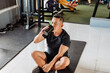 © Mdv Edwards - Southeast Asian man in his 50s sits on gym mat, drinking water or sports drink post ab workout, recovering and hydrating.