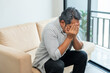 © Chanakon - Asian mature old man sitting headache tired on sofa at home. Portrait of serious depression sadness senior asian man. Mature People Depressed problem in life