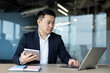 © Tetiana - An asian businessman intently working on his laptop with a tablet in a modern office.