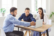 © Studio Romantic - Young family couple sitting at desk with realtor, looking at laptop screen, choosing new house. Husband and wife exploring real estate options for purchase or rent with professional real estate agent.