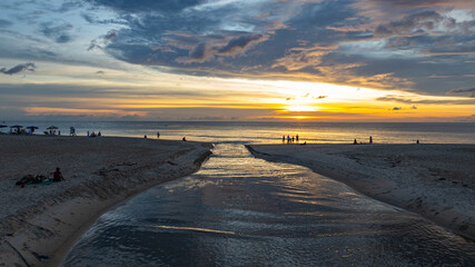 Wall Mural - The water from the canal flows to meet with the sea water..Golden sparkles in the sky shine in the water silhouette on the beach..The reflection of yellow sky shines on the beach.