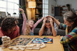 © pressmaster - Family gathered around table, celebrating a win during competitive board game night, with expressions of joy and camaraderie evident. Homey background filled with cozy details
