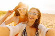 © maxbelchenko - Two happy women with a bouquet of flowers pose for a selfie on a sandy beach. Beautiful friends enjoy the weather and a picnic at sunset and take photos on their phones. Blogging, leisure concept.