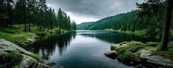 Poster - Scenic view of lake in pine forest under cloudy blue sky concept. Serene lake surrounded by lush green forest under dark clouds.