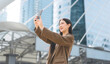 © dodotone - Happy asian business woman using smartphone standing in city