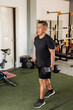 © Mdv Edwards - Middle-aged Southeast Asian man carries two dumbbells in a farmer’s walk for forearm or grip strength and endurance training inside open-air gym.