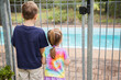 © Austockphoto - Two young kids looking through pool fence bars