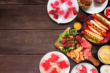 Fototapete - Canada Day patriotic food. Top down view side border on a dark wood background. Hot dogs, hamburgers and maple leaf red and white theme snacks. Copy space.