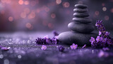 Smooth black spa stones stacked in balance surrounded by purple lavender flowers on glittery surface with dreamy bokeh lights
