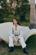 © SHOTPRIME STUDIO - Business woman in light suit sitting on modern bench outdoors, thoughtful expression, green park background, stylish fashion portrait, spring season