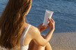 © Daryna  - Young woman with flowing hair holding and opens a white mockup tube of cream on the background of sea waves on the beach. The concept of cosmetics for body skin care, sunscreen, beauty products.