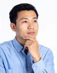 Wall Mural - Thoughtful Asian man with hand on his chin, wearing blue shirt, poses against clean white studio background