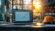 © zong - Laptop displaying building architectural blueprint on desk with yellow hard hat and pencils in warm sunset light inside modern office