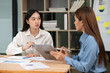 © Thitisak - Two Asian businesswomen holding graph papers are sitting and talking happily while working.