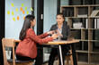 © Thitisak - Two Asian businesswomen with laptops discussing documents in an office.