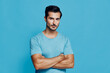 © SHOTPRIME STUDIO - Confident young man with strong build wearing a light blue t-shirt, standing against a solid blue background with arms crossed, looking directly at the camera.