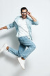 © SHOTPRIME STUDIO - Full body joyful happy young man wearing casual blue shirt and jeans jumping playfully while smiling at the camera isolated on clean white background. Lifestyle concept
