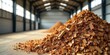 © araet - A large pile of fragmented wood pieces rests on a concrete floor inside a spacious industrial building with tall windows.