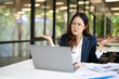 © maeching - Asian businesswoman working on financial market research using laptop and digital tablet, stressed about digital investment in office.
