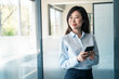 © Stock 4 You - Asian young business woman manager using cell phone mobile app standing in office. 40s middle age female businesswoman working on smartphone cellphone application, looking aside dreaming. Copy space