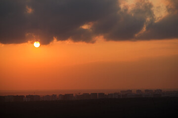 Wall Mural - Sunset over city skyline with dark clouds. Urban landscape with orange sky and setting sun. Cityscape photography with copy space.