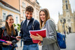 © Mediteraneo - Group of Three Students Studying Together with Books and Tablet While Walking Outdoors..