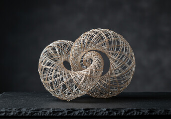 Poster - Abstract sculpture: decorative wire design on dark background features intricate interwoven pattern and spiral form creating a visually compelling piece of art