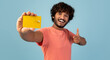 © Prostock-studio - Cheerful handsome young indian man holding yellow credit card and showing thumb up, pleased client demonstrating bank product over blue studio background, panorama. Finance, loan, savings concept