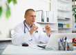 © JackF - Focused doctor sitting at table in medical office, talking to webcam on laptop, conducting online patient consultation