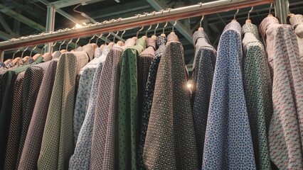 Poster - A rack of clothes with a variety of patterns and colors, including green, blue, and white. The clothes are hanging on a rack, and the colors and patterns are diverse
