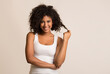 © Prostock-studio - Smiling african-american woman flirting and touching her curly hair over light background