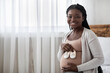 © Prostock-studio - Black Pregnant Woman Preparing For Motherhood, Holding Small Baby Shoes Near Belly, Happy Awaiting African American Lady Sitting On Bed And Smiling At Camera, Enjoying Maternity, Copy Space
