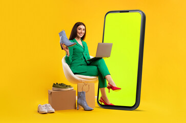 Poster - Mobile shopping concept. Lady sitting near giant cellphone and holding new shoes, buying online over yellow background. Fashion and style application. Mockup