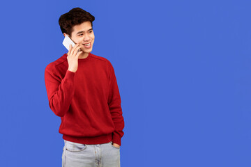Poster - Always In Touch. Portrait of casual smiling asian guy talking on his smartphone, looking aside, standing and posing isolated over blue studio background, banner, copy space. Communication, Phone Call