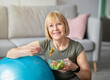 © Prostock-studio - Exercise and healthy diet concept. Senior woman with fitball eating fresh vegetable salad at home. Mature Caucasian lady having veggies after sports training, keeping weight loss diet