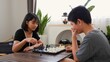 © FAMILY STOCK - Asian teenage boy and girl playing chess at home, developing strategic thinking, logic, and concentration. Concept of brain training, youth education, and indoor board game activity.