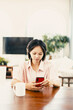 © VERSUSstudio - Young asian female using smartphone in modern home interior