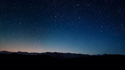 Wall Mural - a a movement of stars in the night sky with the view of mountains.