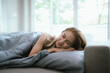 © Natthawadee - A young woman wakes up in a cozy bedroom, stretching on a comfortable bed with sunlight streaming in, enjoying peaceful relaxation.
