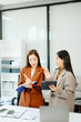 © Nuttapong punna - Two Asian businesswomen discuss ideas and documents at the office desk, showcasing teamwork, leadership, and corporate planning