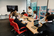 © Drobot Dean - The multiracial adult men and women sit around a large conference table during a business meeting in a modern office, with one woman standing and presenting to the group.