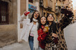 © Drobot Dean - Three besties pose for a joyful street selfie, drinks in hand, radiating confidence and carefree energy in their stylish winter outfits. The concept of youth and women's friendship.