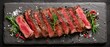 © EchoFrame - Sliced steak presentation on black slate with rosemary and spices, top-down view of medium rare beef fillet for gourmet dining