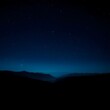 © Beratonic Studios - Distant mountains are silhouetted beneath a vast, dark blue night sky filled with twinkling stars.