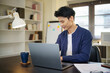 © matinee - Smiling businessman reviewing work on laptop in an office with documents and a coffee cup on the desk.